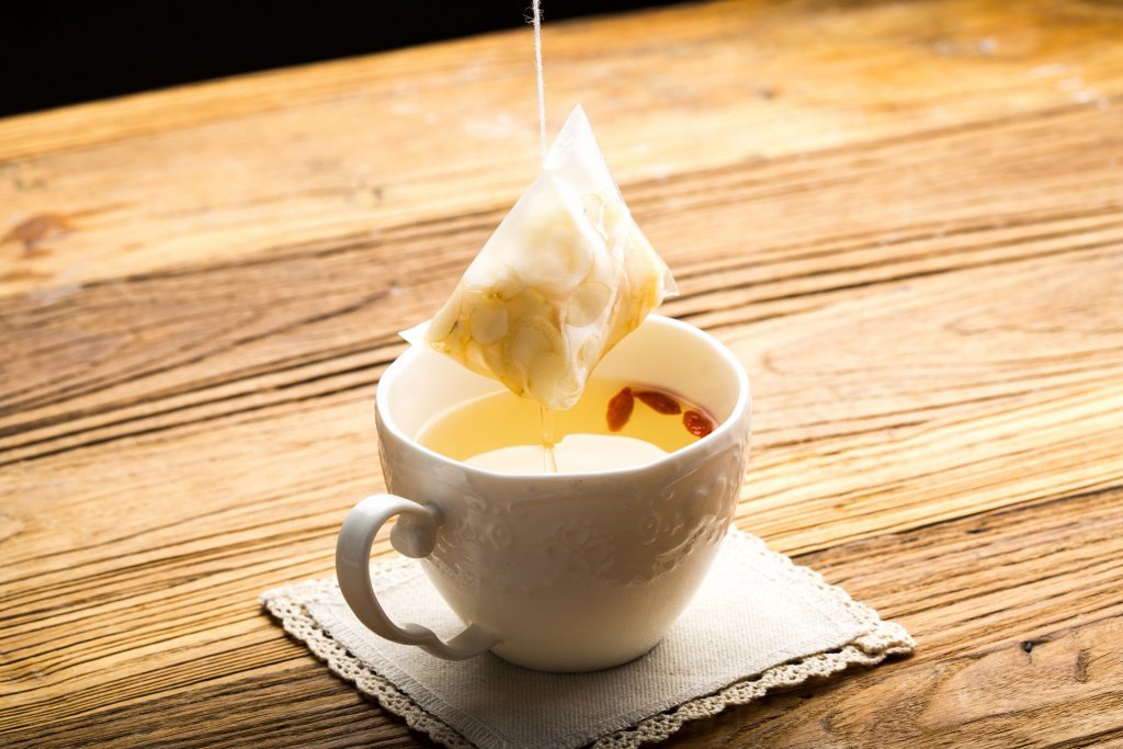 花旗蔘茶包沖泡中，茶湯透亮溫潤，杯中可見枸杞與蔘片